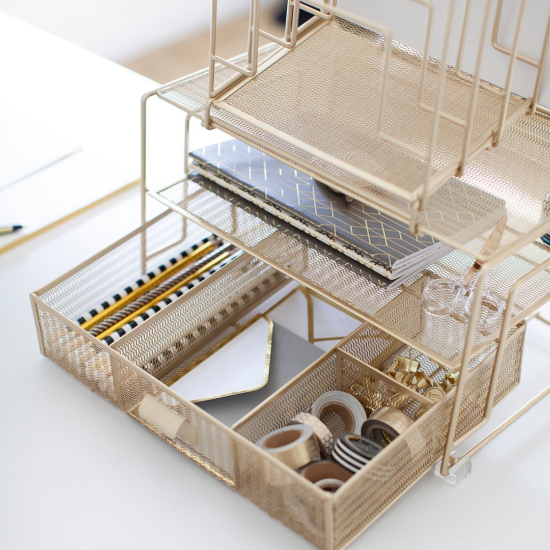 Gold mesh desk organizer with notebooks, pens, envelopes, and washi tape on a white desk.