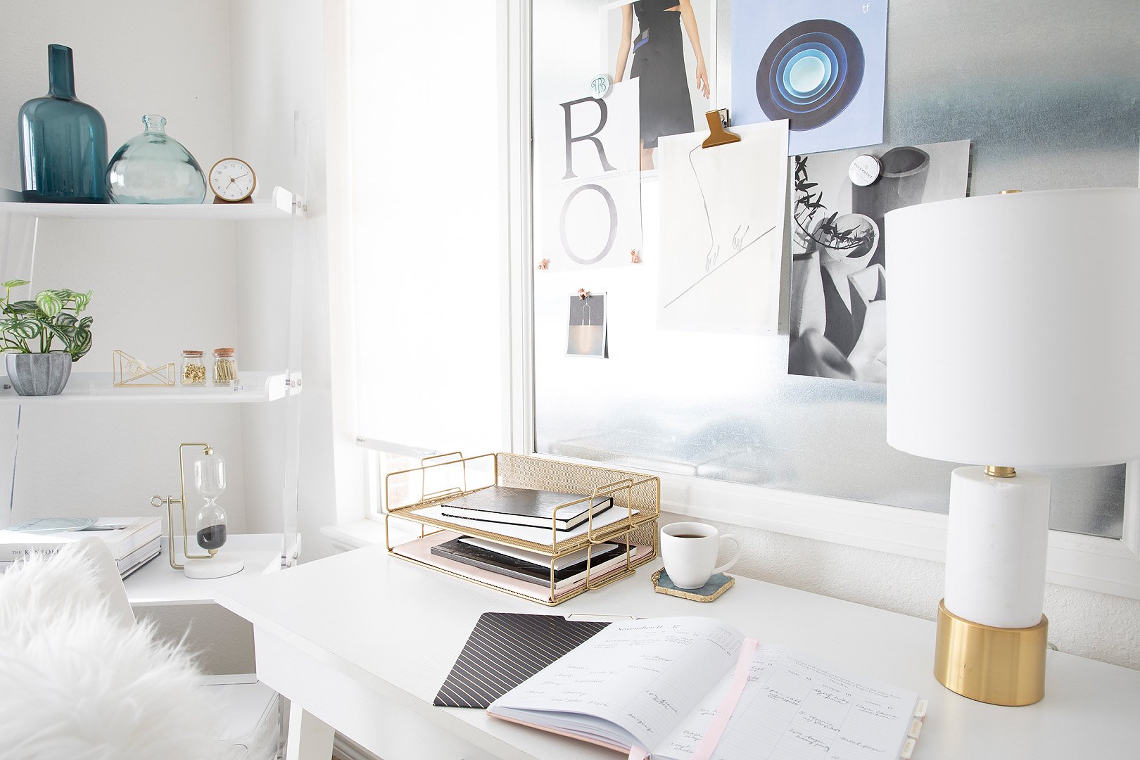A bright and organized workspace featuring a white desk, gold accessories, and a decorative shelving unit.