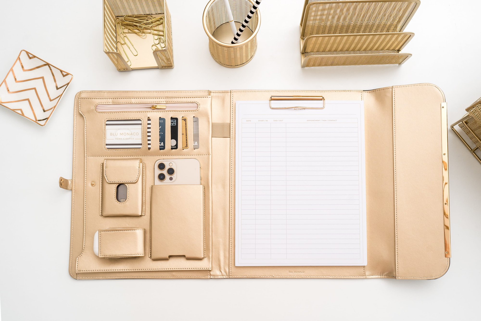 A luxurious flat lay of gold office supplies, featuring a planner with cards, a phone, and desk accessories.