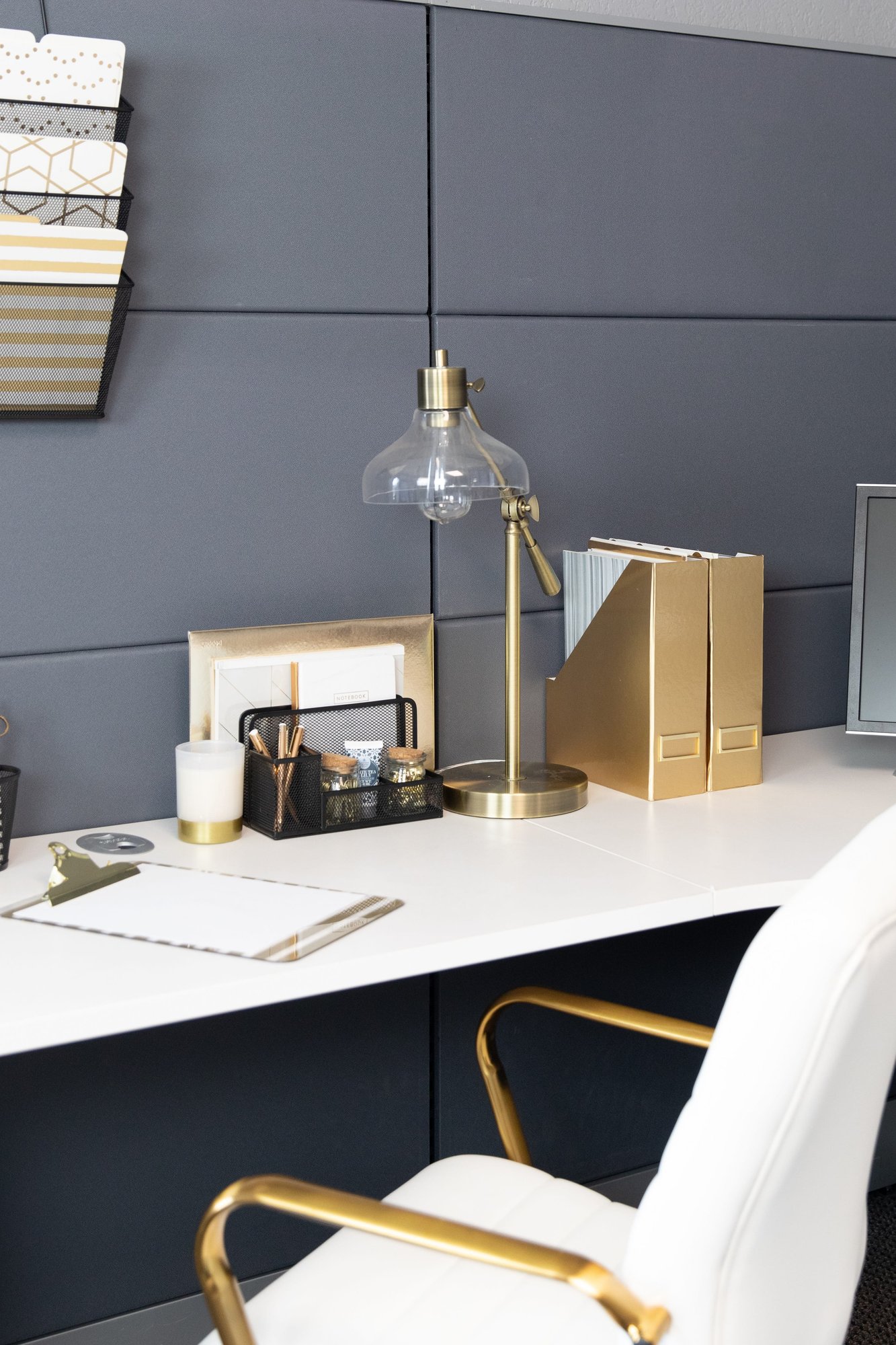 A stylish home office desk featuring gold and black organizers, a lamp, and a white chair.