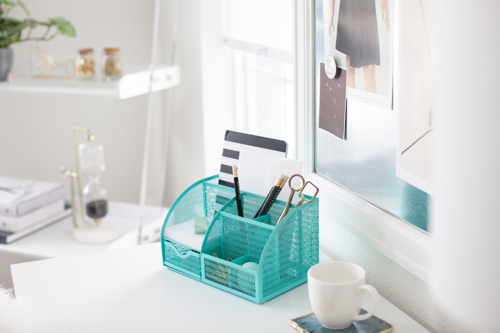 A bright, organized desk with a teal mesh organizer, pencils, and a white mug.
