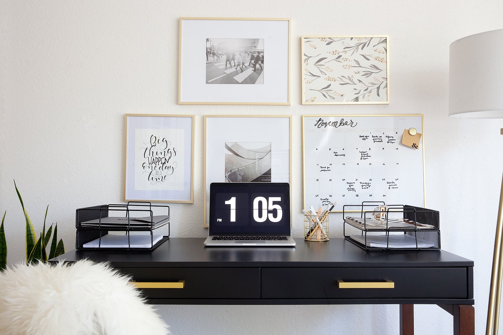 A neatly organized black desk with a laptop, office supplies, and framed art on a white wall.