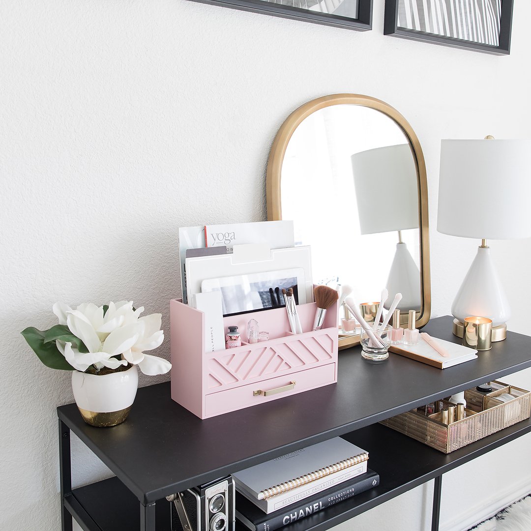 A stylish black console table with a pink desk organizer, mirror, lamp, and decorative accessories.