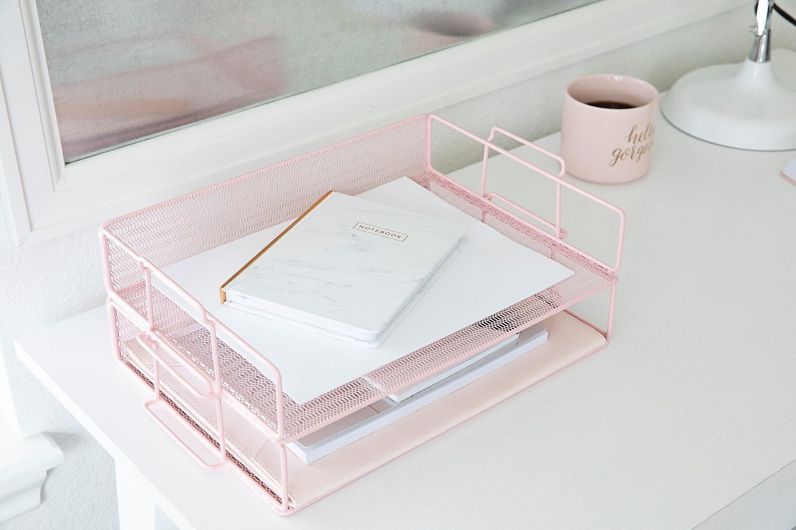 A pink mesh desk organizer holds a marble notebook and papers on a white desk with a pink mug.