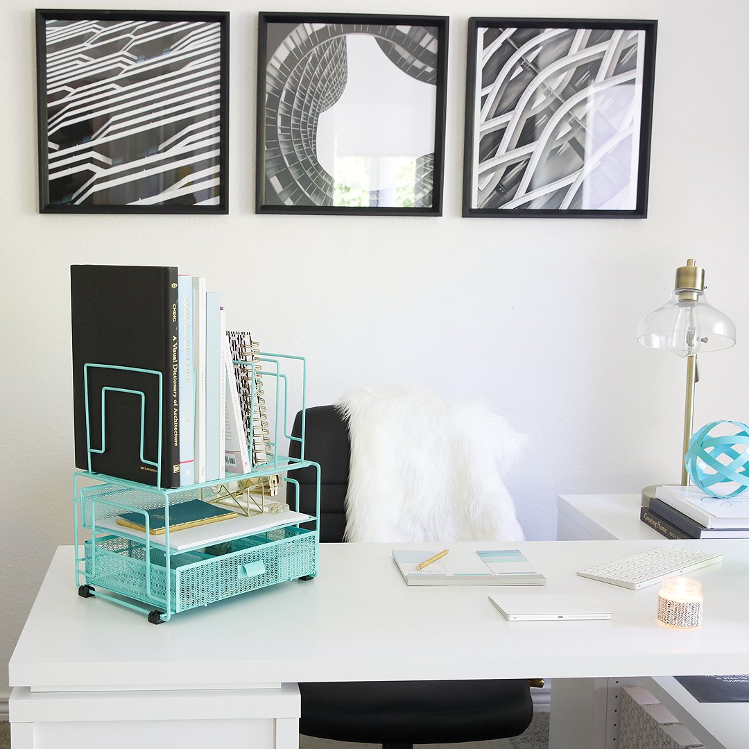 A neatly organized white desk in a home office with a teal organizer and framed art.