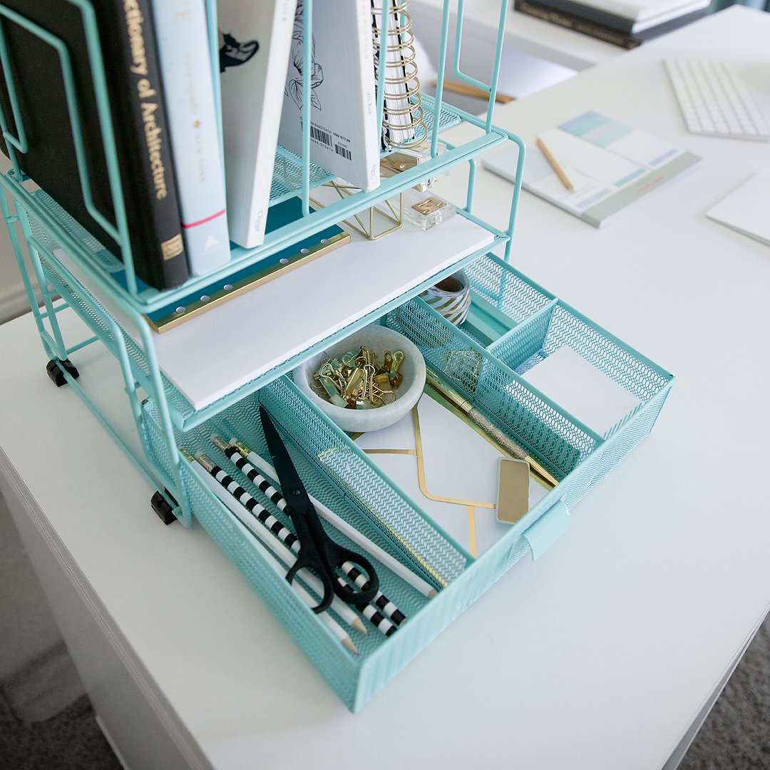 A light blue mesh desk organizer filled with books, notebooks, and a drawer of office supplies.