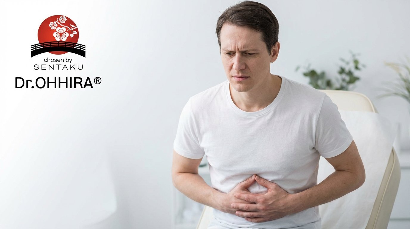 Mies valkoisessa t-paidassa pitelee vatsaansa tuskallisesti, ilmeessä kipua tai epämukavuutta.