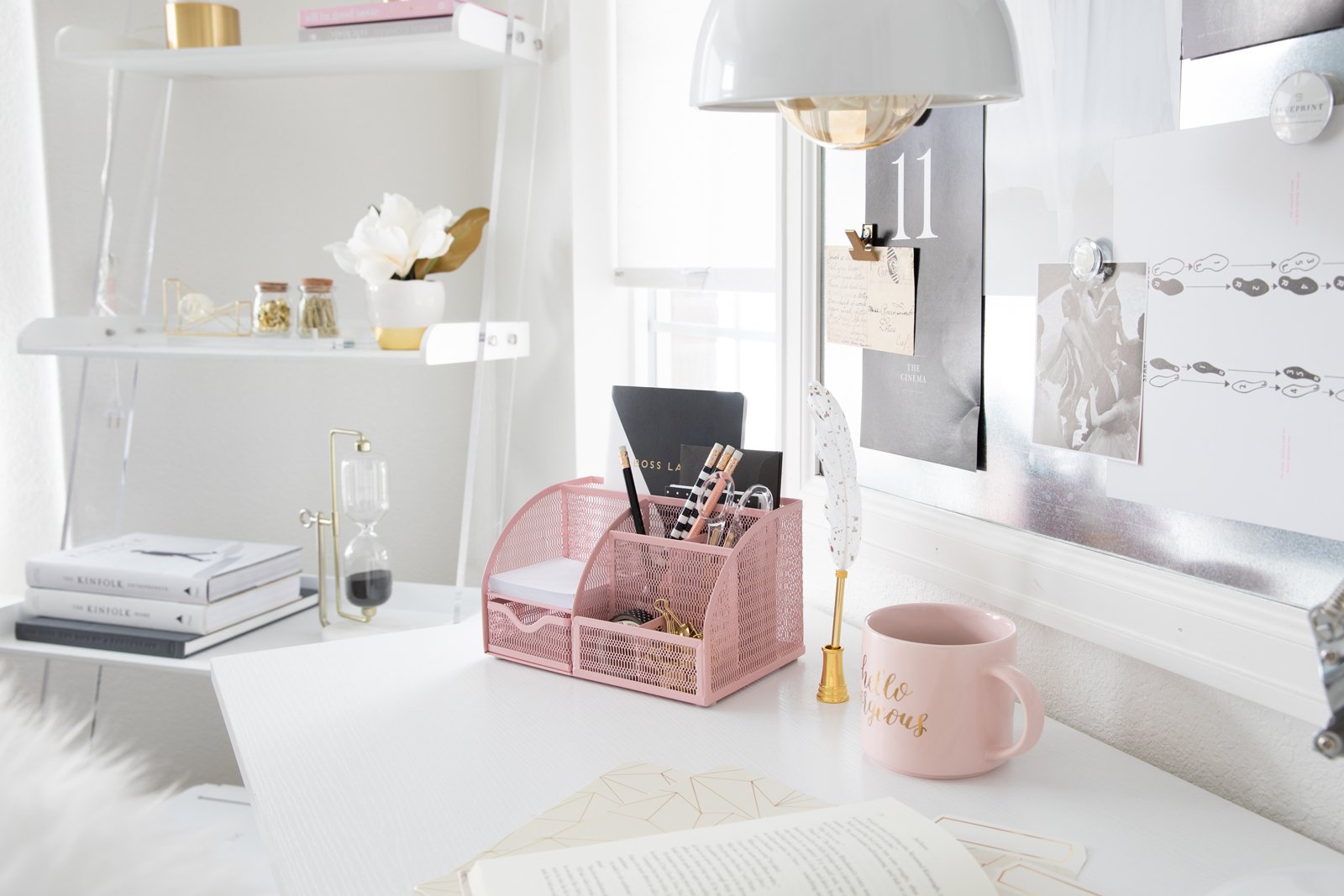 A bright, clean home office desk with a pink organizer, a mug, and books.