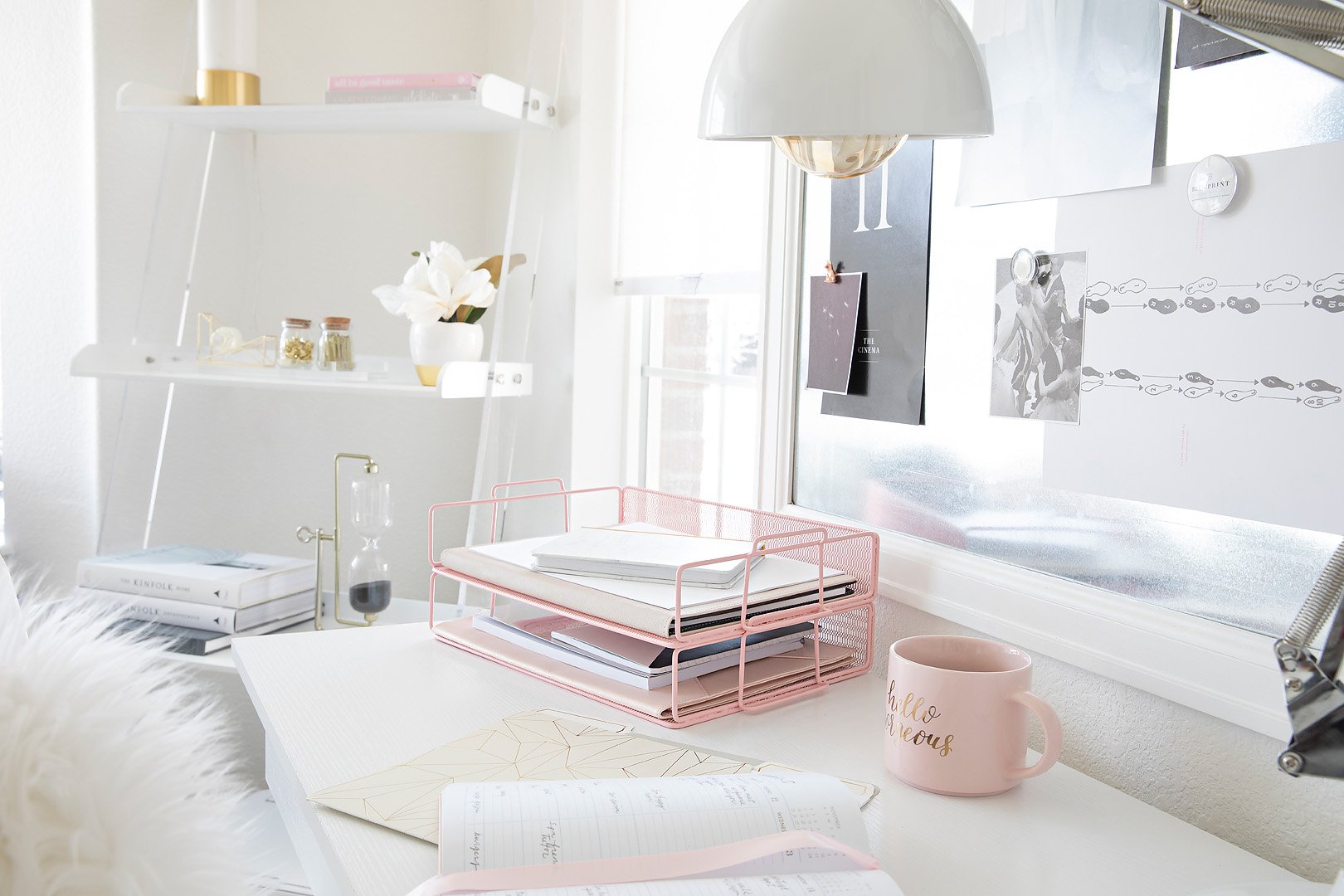 A bright and tidy home office desk with pink organizers, books, and decorative items.