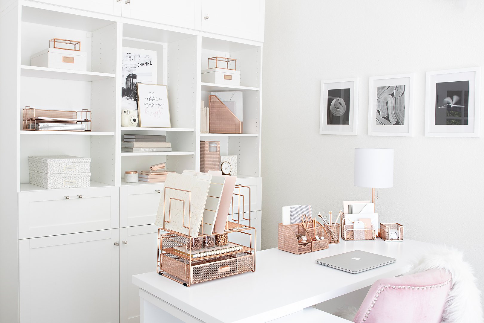 A clean, organized home office featuring white built-in shelves, a desk, and rose gold office supplies.