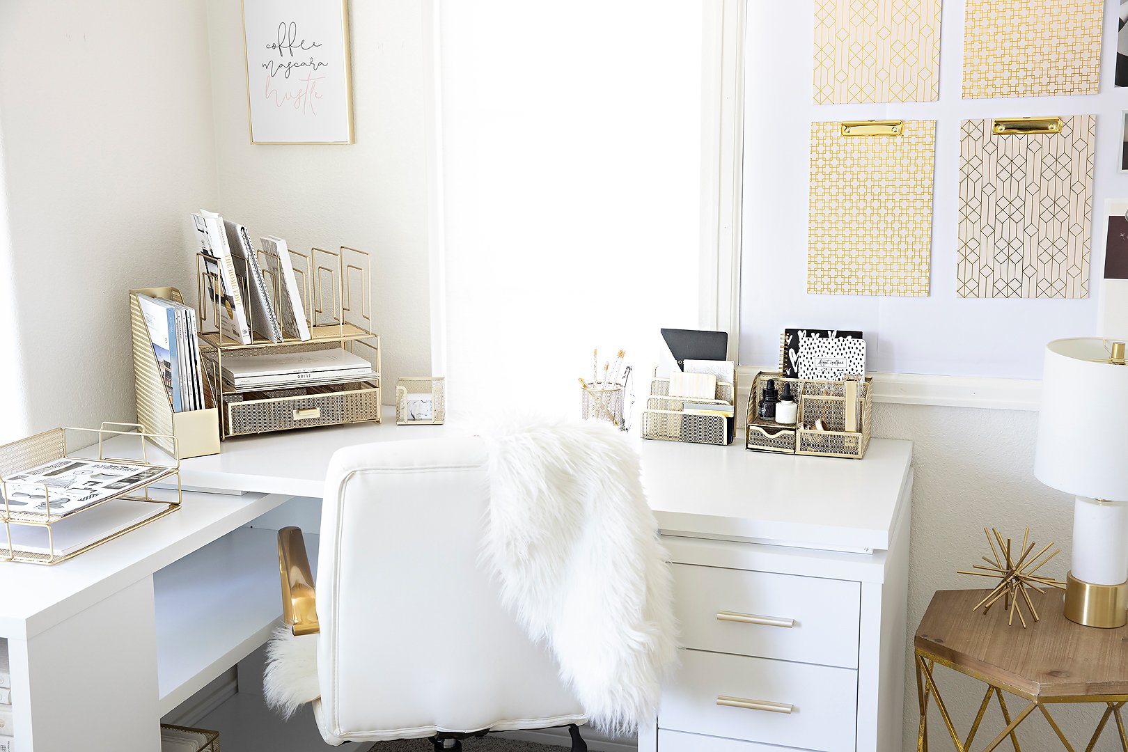 A bright, organized L-shaped home office with white furniture and gold desk accessories.