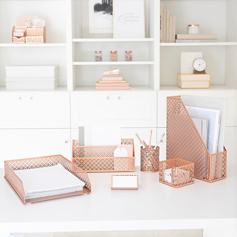 A clean home office features a desk with a rose gold geometric metal stationery set and decorative shelves.