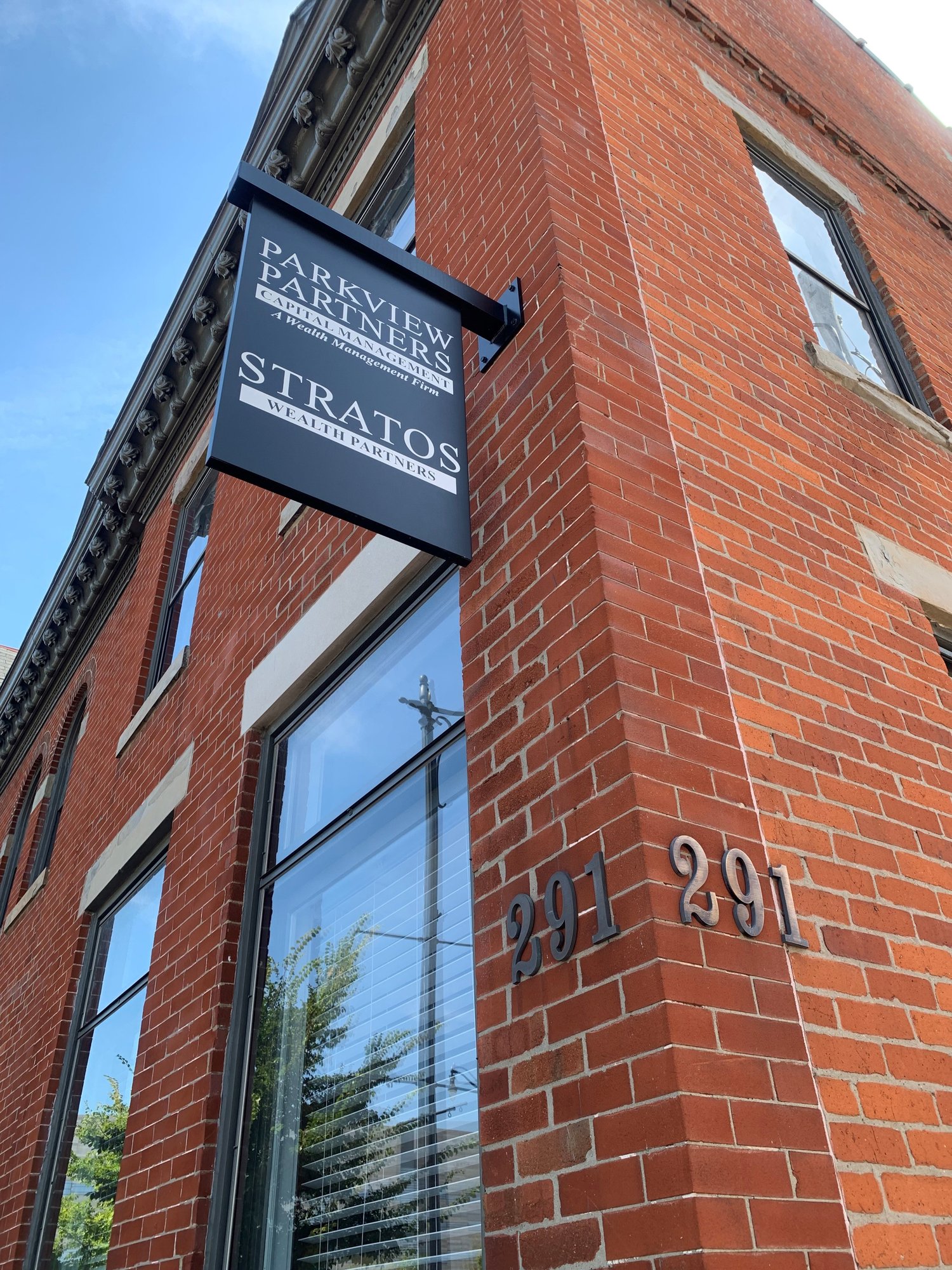 A red brick building with a black sign for Parkview Partners and Stratos Wealth Partners, displaying the address 291.