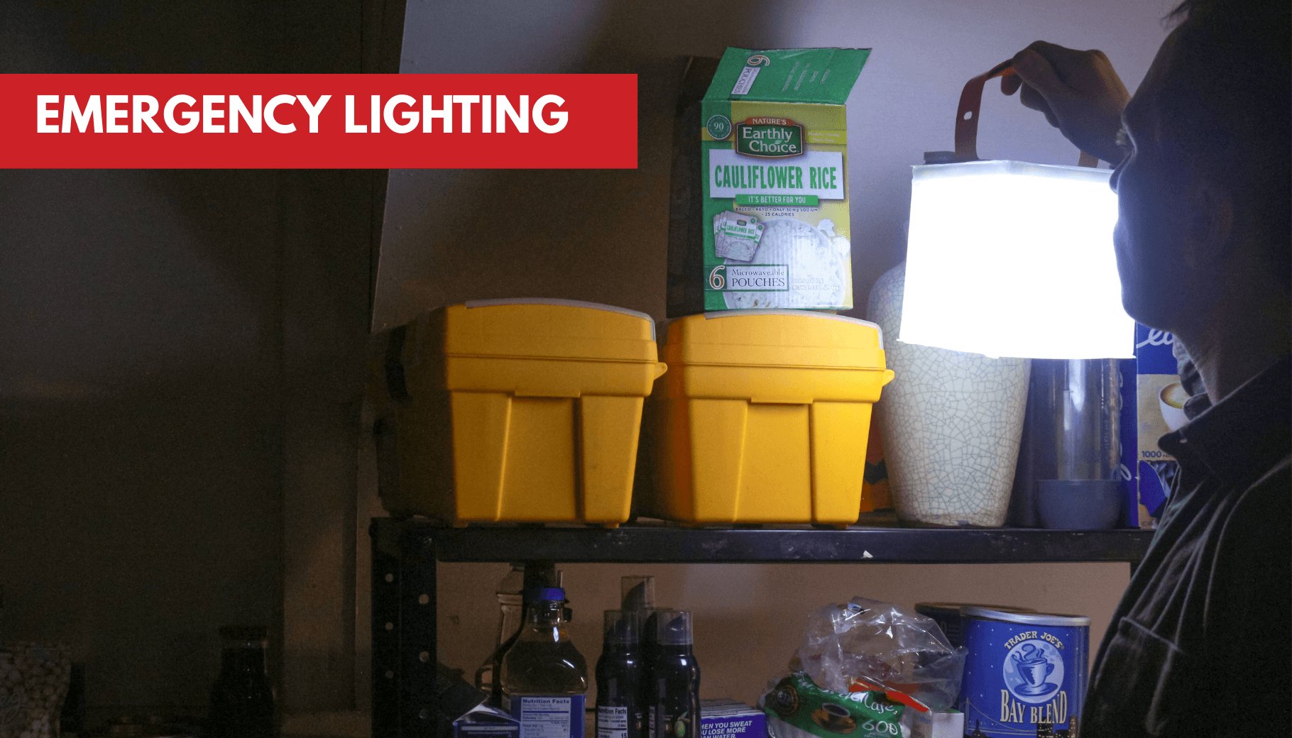 A person holds a bright white lantern illuminating a shelf with emergency food and supplies.