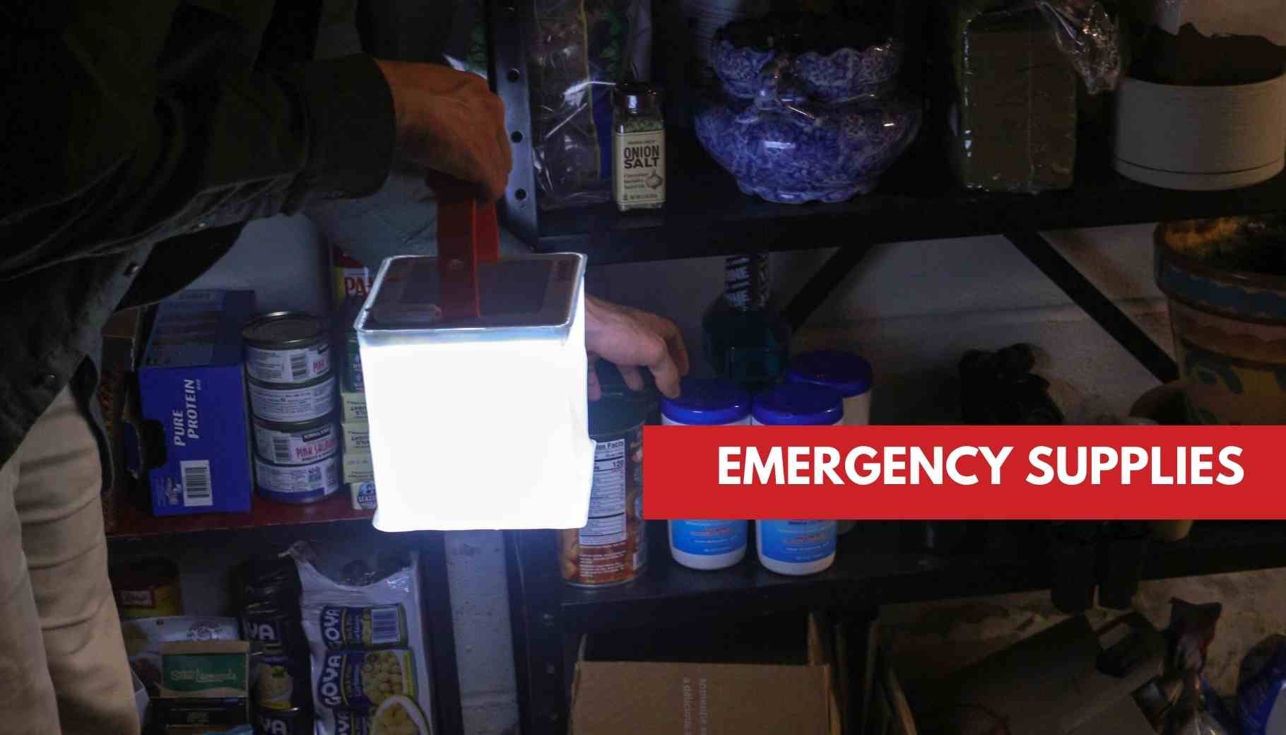 A person holds a bright lantern, illuminating shelves stocked with emergency food and supplies.