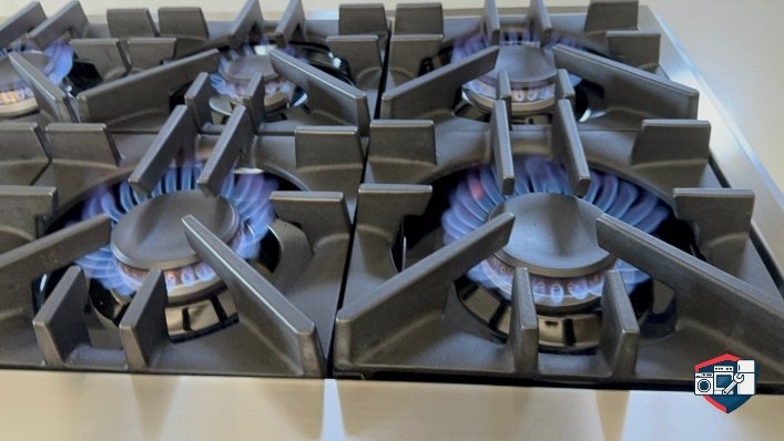 Close-up of a modern gas range with multiple burners lit, showing blue flames.