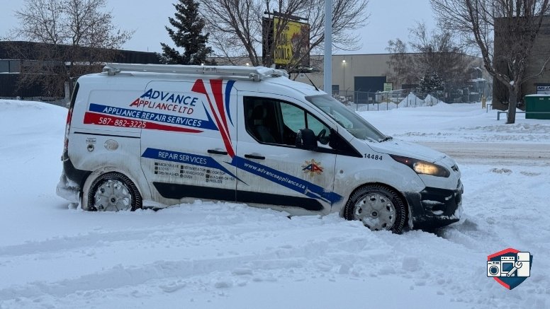 A white Advance Appliance Ltd. service van is stuck in deep snow on a winter day.