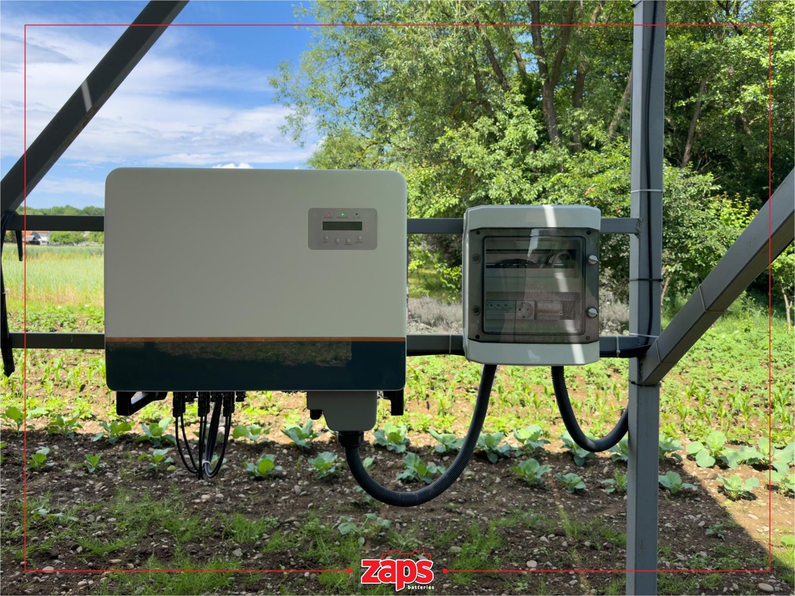 Φωτοβολταϊκός μετατροπέας και ηλεκτρικός πίνακας σε εξωτερικό χώρο, δίπλα σε κήπο με λαχανικά και δέντρα.