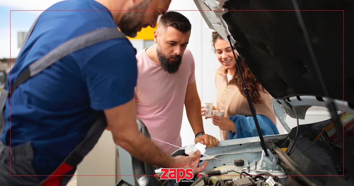 Ένας μηχανικός ελέγχει τον κινητήρα ενός αυτοκινήτου, ενώ δύο πελάτες παρακολουθούν.