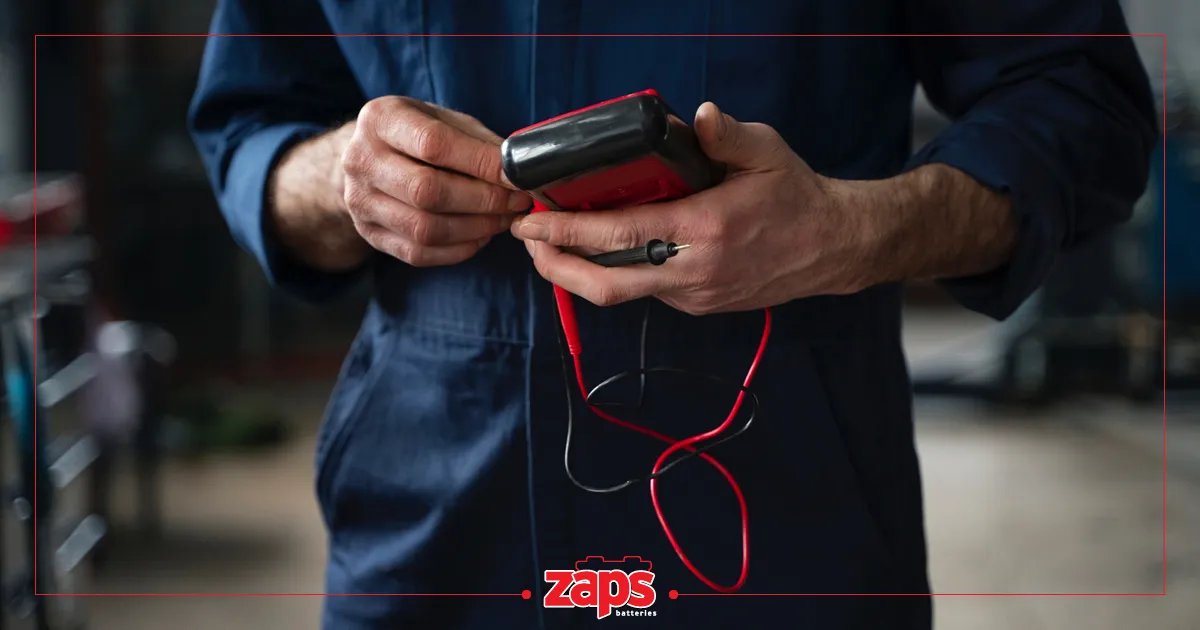 Ανδρικά χέρια με μπλε φόρμα κρατούν ένα κόκκινο πολύμετρο με καλώδια, ετοιμάζοντας το για χρήση.