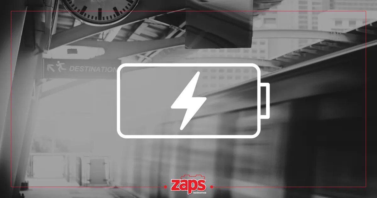 Μια μεγάλη λευκή μπαταρία με κεραυνό σε φόντο σταθμού ή αεροδρομίου με πινακίδα 'ΠΡΟΟΡΙΣΜΟΣ'.