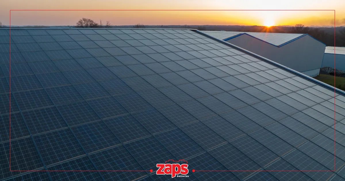 Μεγάλη στέγη καλυμμένη με ηλιακά πάνελ, με το ηλιοβασίλεμα να φωτίζει τον ορίζοντα και άλλα κτίρια.