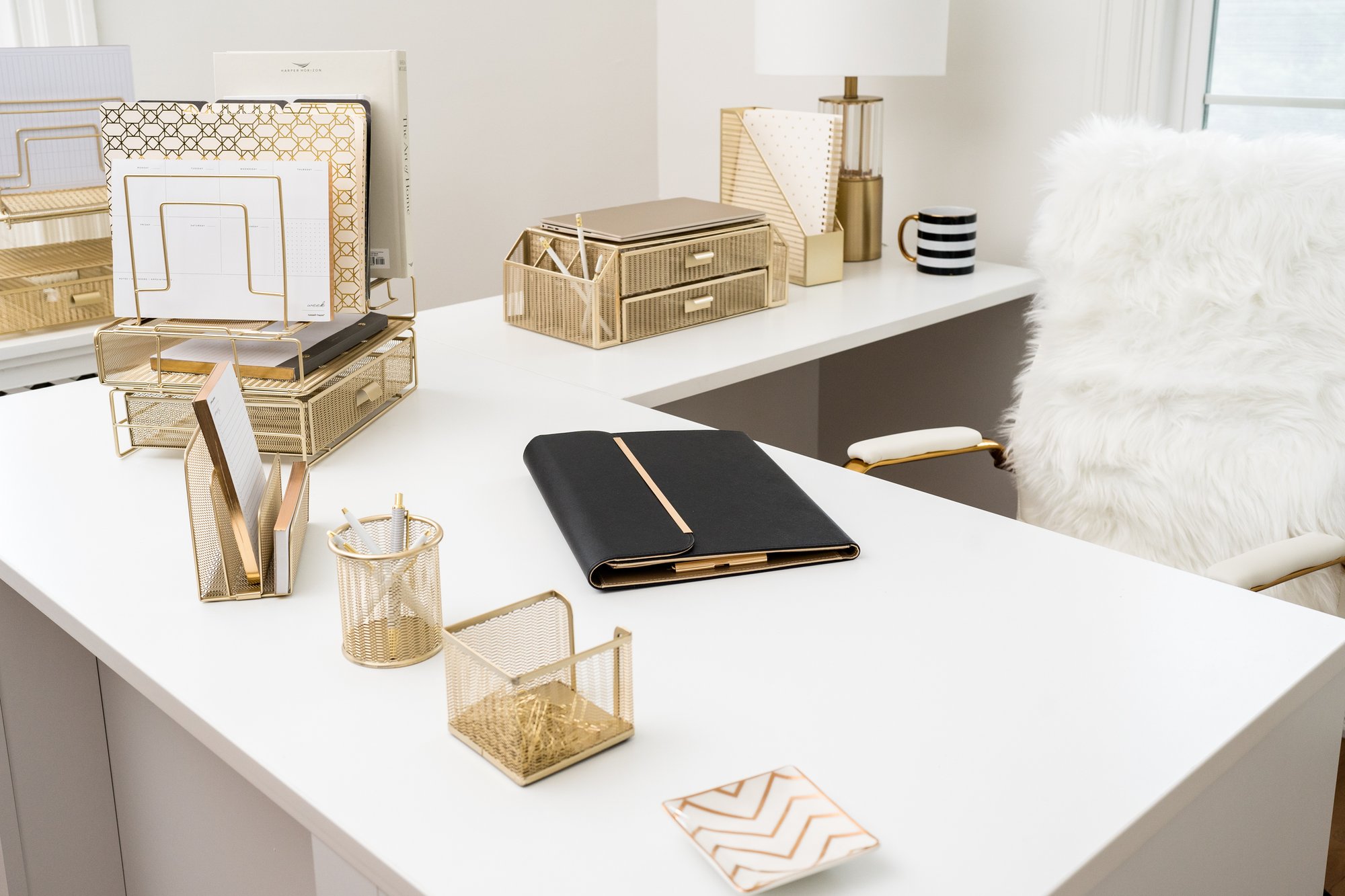 A bright, elegant home office desk featuring various gold mesh organizers and decorative items.