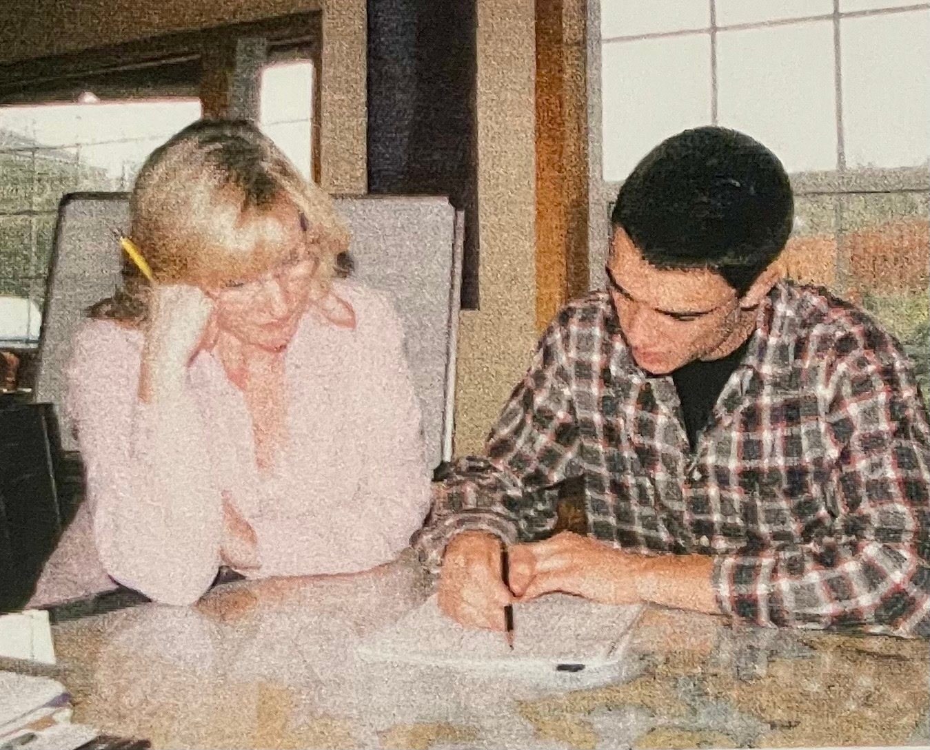 Two people, a blonde woman and a man in a plaid shirt, studying at a table.