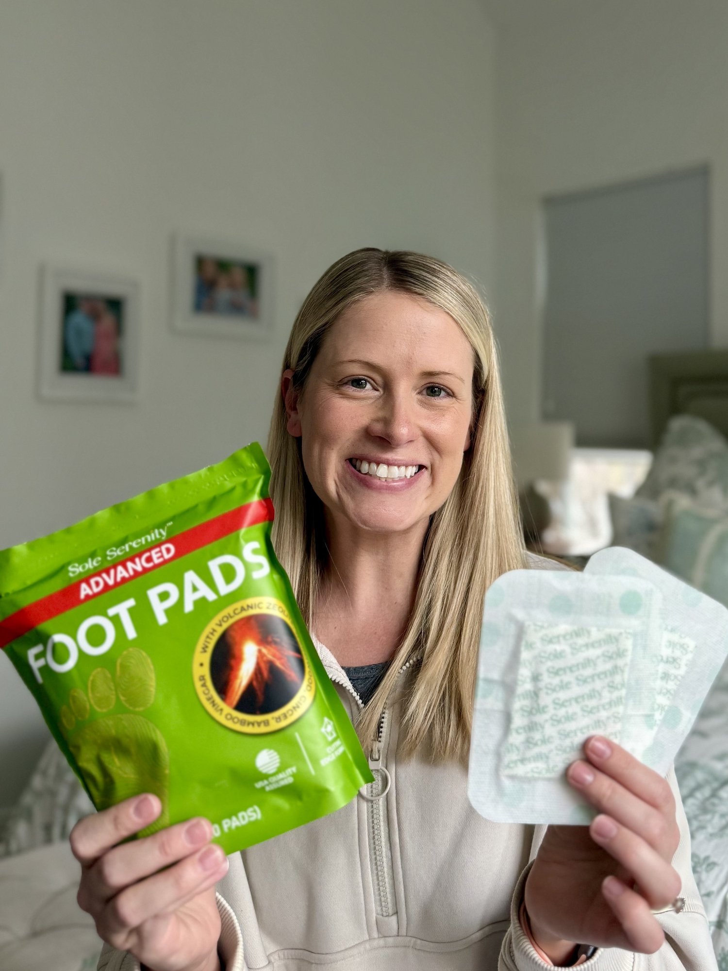 A smiling blonde woman holds a green bag of "Sole Serenity ADVANCED FOOT PADS" and two white foot pads.