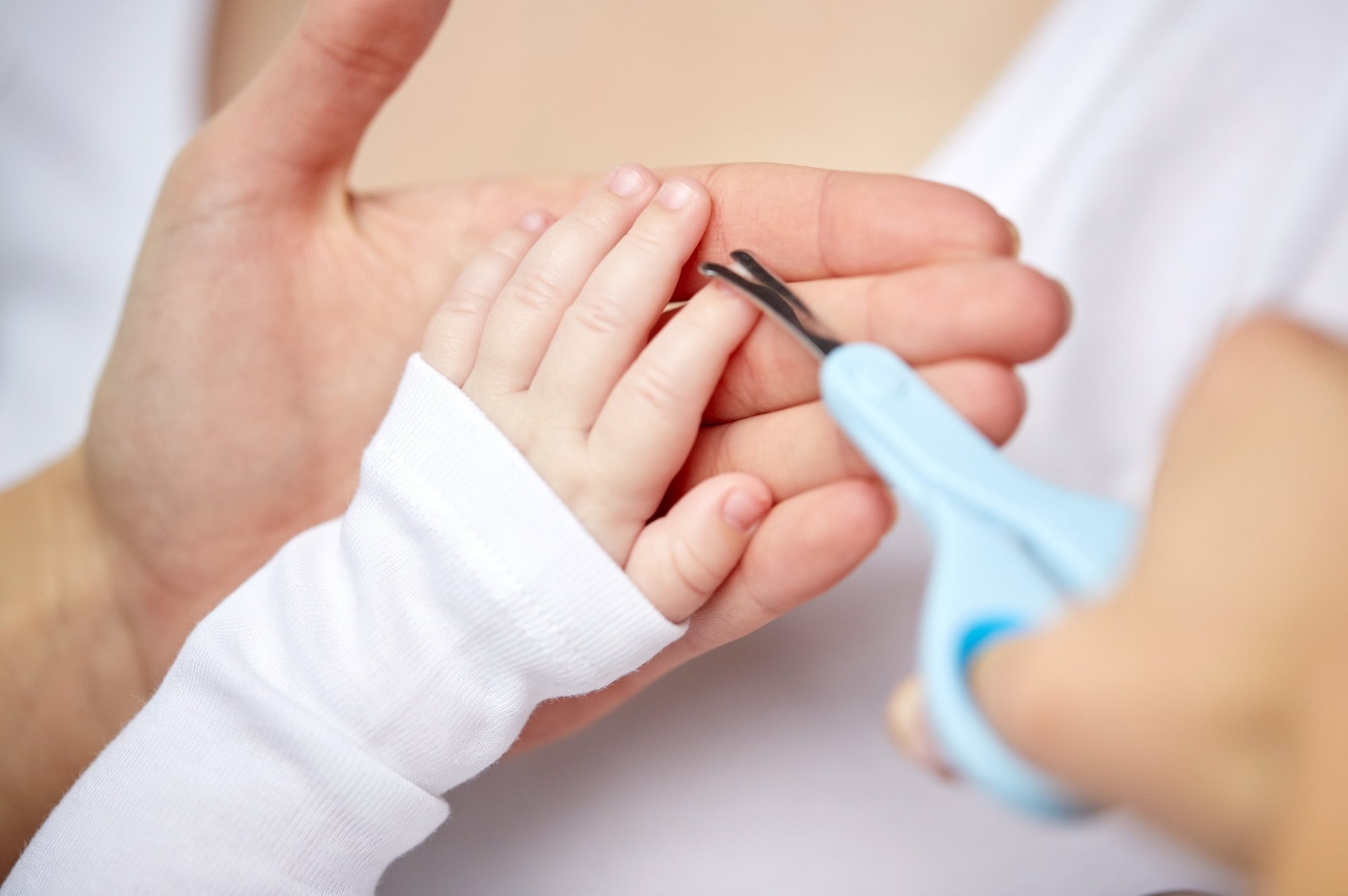A close-up shows an adult carefully trimming a baby's fingernails with blue safety scissors.