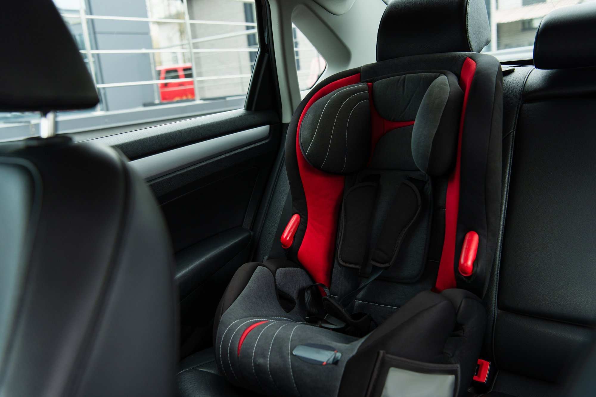 A red and black Baby Trend Car Seat is securely placed in the back of a black car.