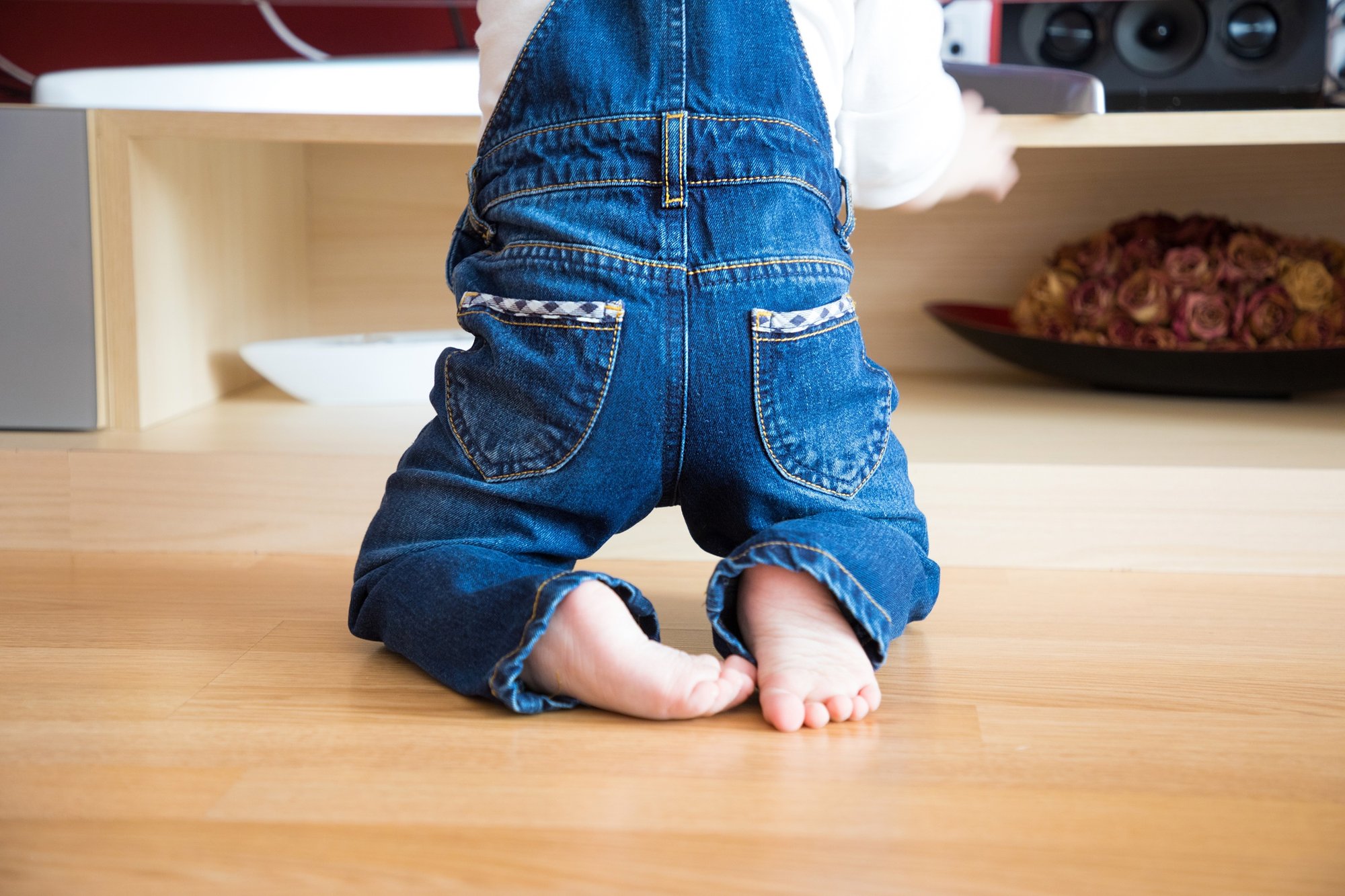 A toddler in toddler boy jeans kneels on a wooden floor, reaching for a shelf.