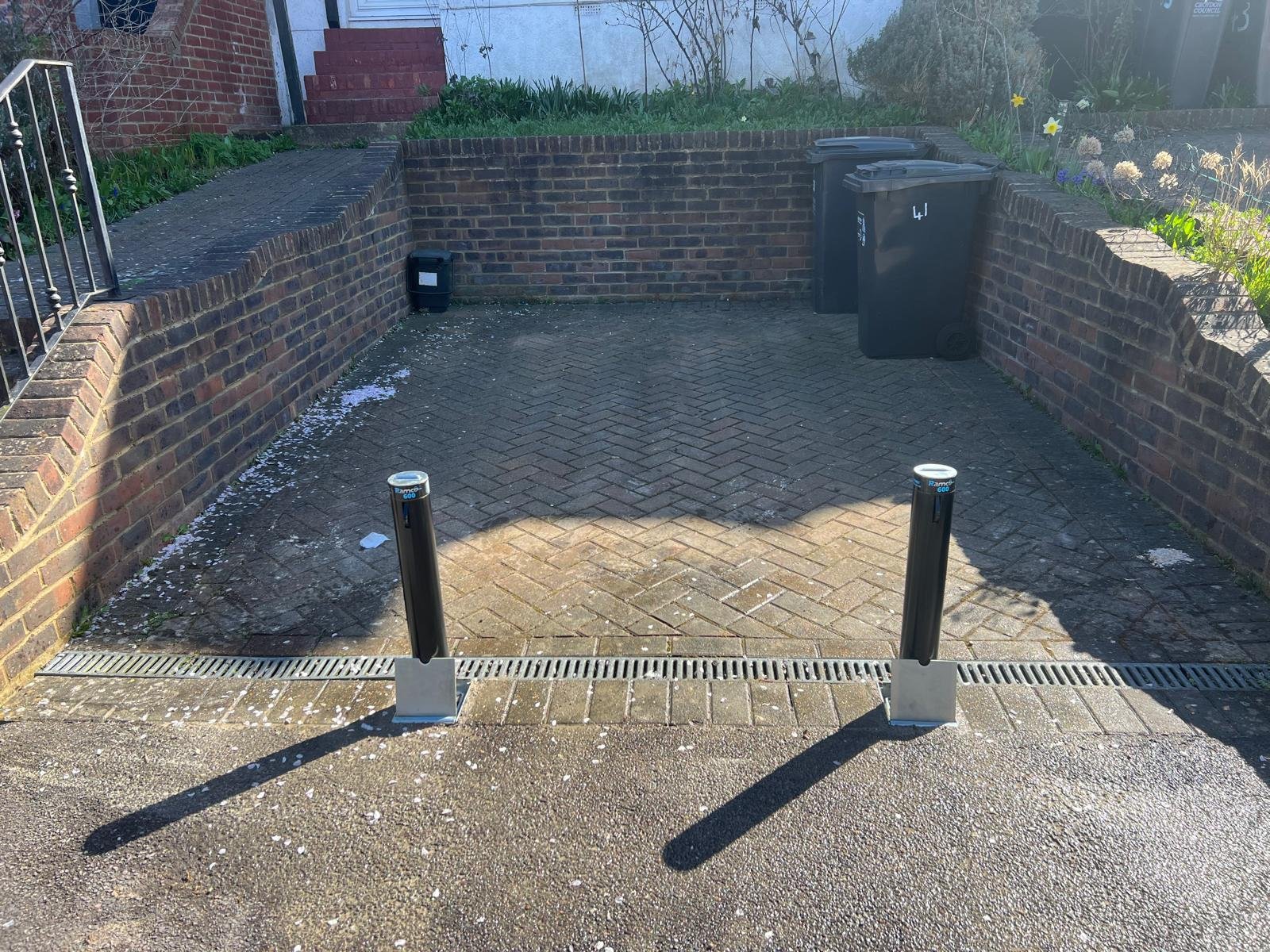 A neatly installed telescopic security bollard, flush with the block paving of a residential driveway.