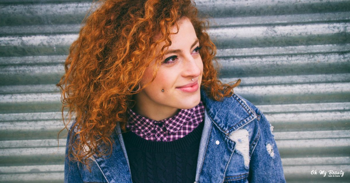 Τα Καλύτερα Προϊόντα για Σγουρά Μαλλιά που θα Λατρέψεις Γυναίκα με πορτοκαλί σγουρά μαλλιά χαμογελά φορώντας τζιν τζάκετ και καρό πουκάμισο