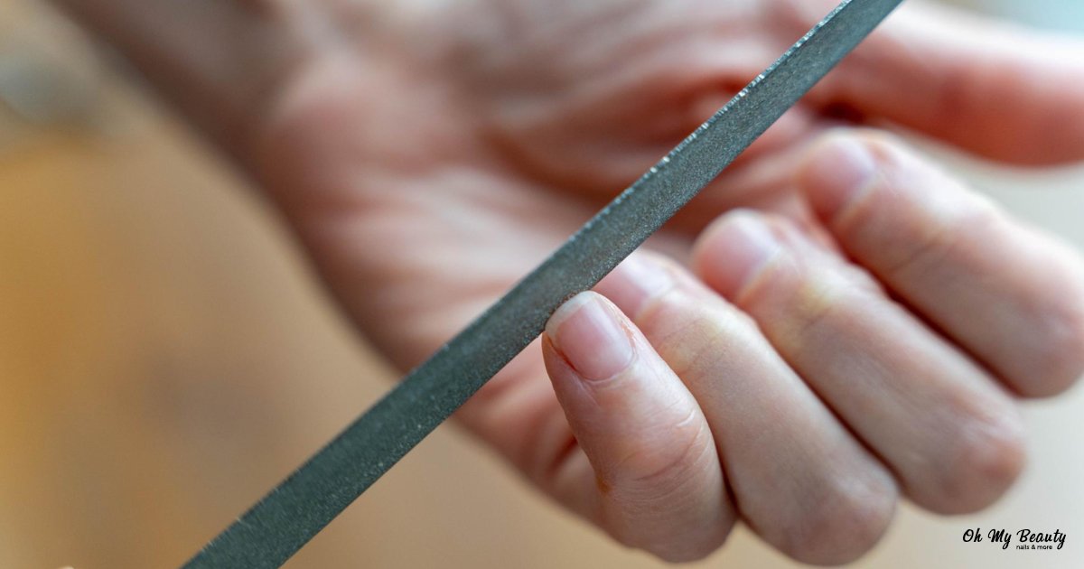 Γραμμές στα νύχια: Ο Απόλυτος Οδηγός για Υγιή & Λαμπερά Άκρα Ένα χέρι κρατάει μια λίμα νυχιών, φροντίζοντας τα νύχια. Κοντινό πλάνο περιποίησης.