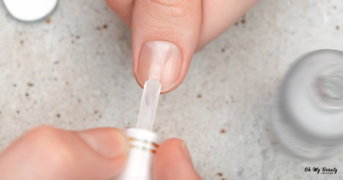 Γραμμές στα νύχια: Ο Απόλυτος Οδηγός για Υγιή & Λαμπερά Άκρα Κοντινό πλάνο ενός ατόμου που εφαρμόζει διαφανές βερνίκι νυχιών σε ένα φυσικό νύχι. Το χέρι κρατάει το πινέλο του βερνικιού.