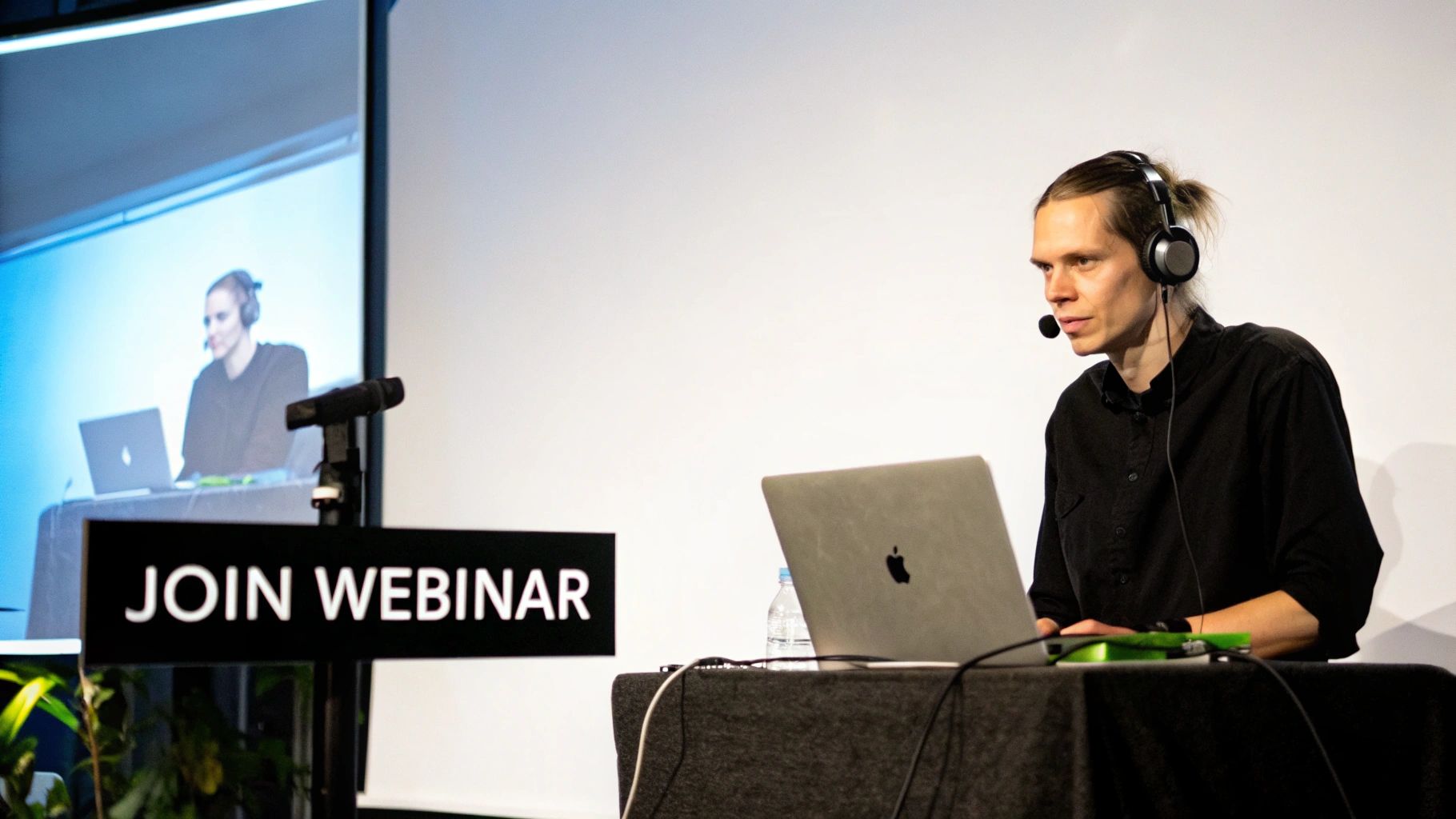A person wearing a headset with a microphone, using a laptop for an online webinar presentation, next to a 'JOIN WEBINAR' sign.