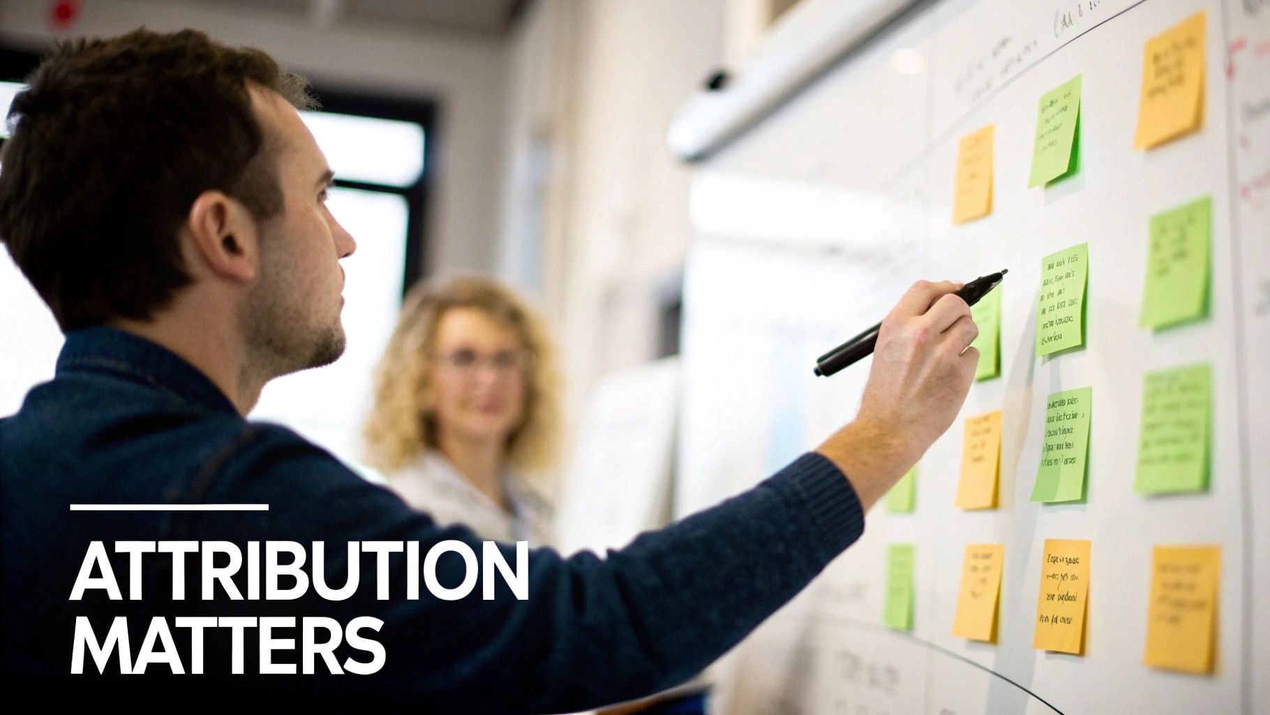 A man writes on a whiteboard covered with green and yellow sticky notes during a brainstorming session.
