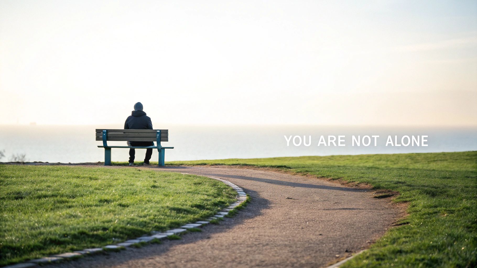 Person sitting alone on a park bench overlooking the sea with the message 