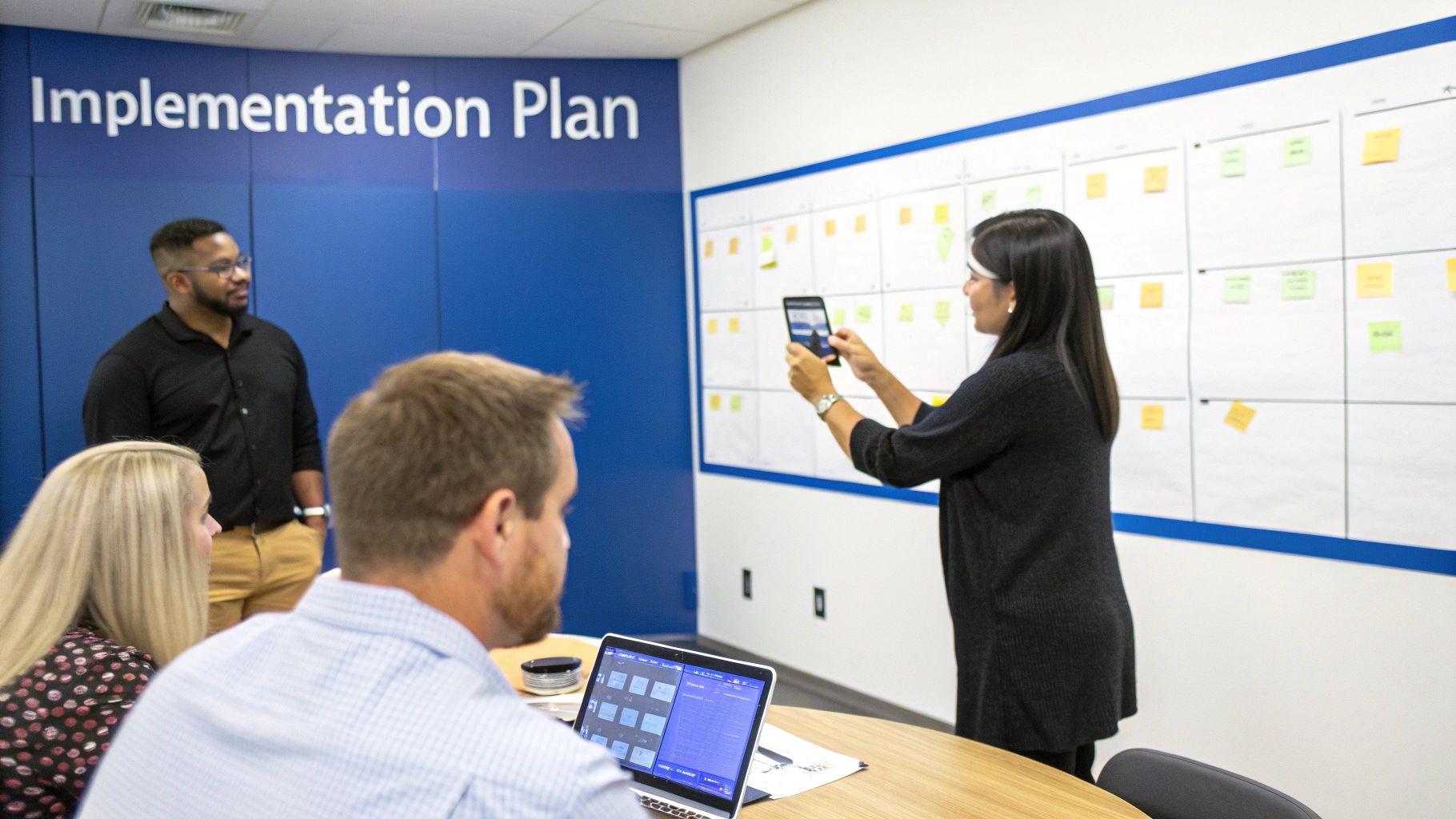 Diverse team collaborating in an office, reviewing an implementation plan on a whiteboard.