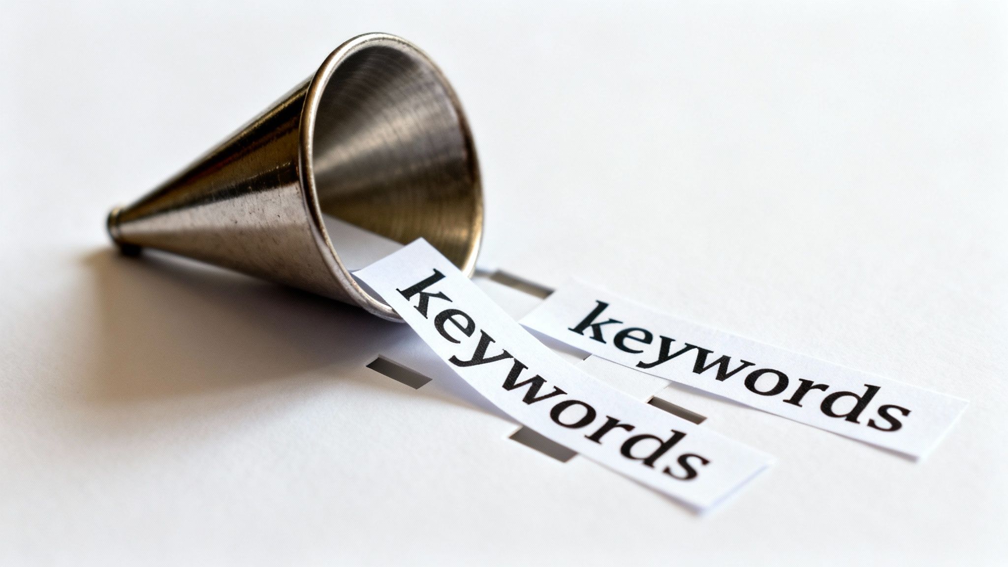 A small silver megaphone or funnel lying down, with strips of paper labeled 'keywords' spilling out.