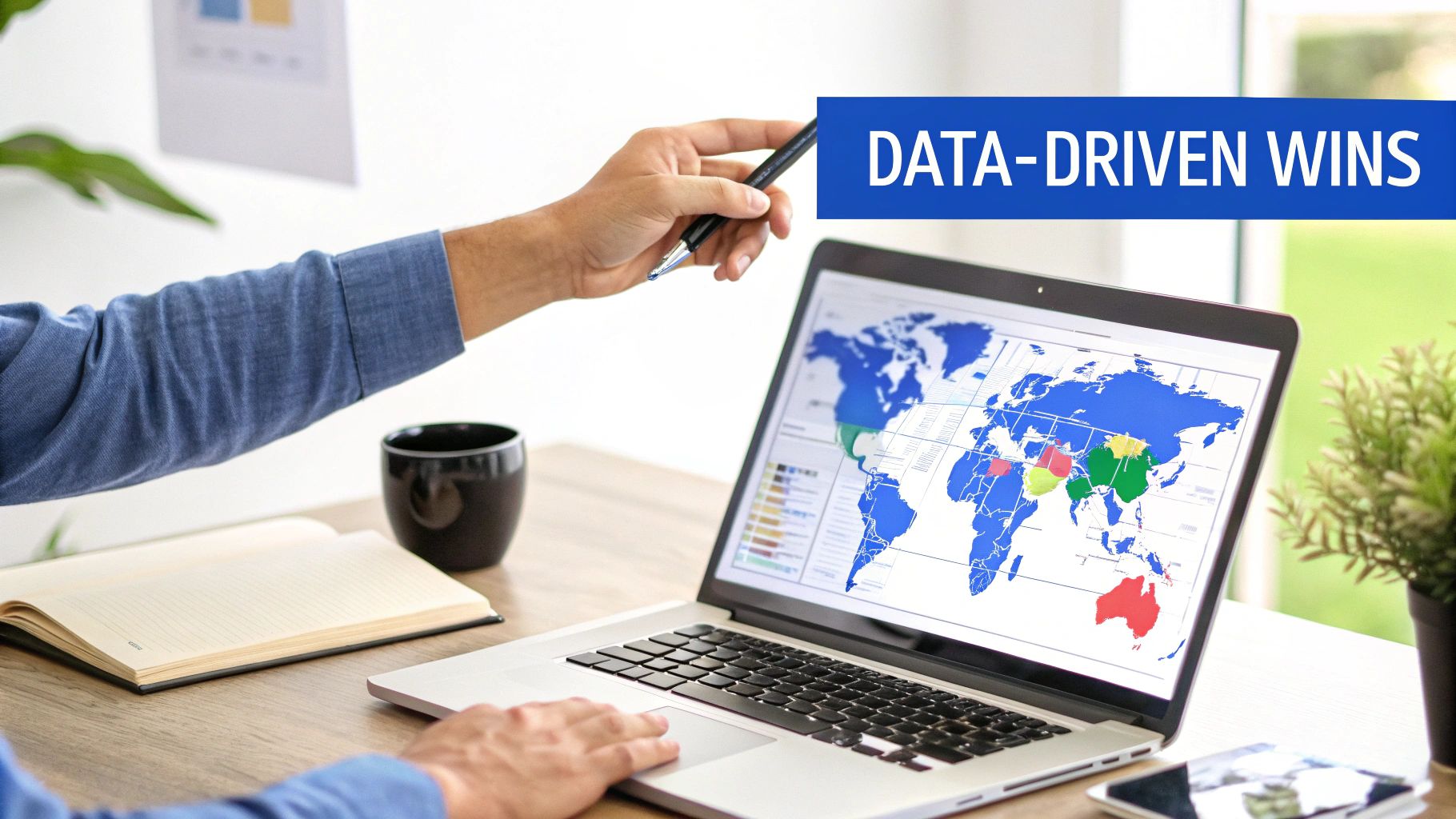 A person's hands point at a laptop displaying a colorful data analytics world map, with a coffee cup.