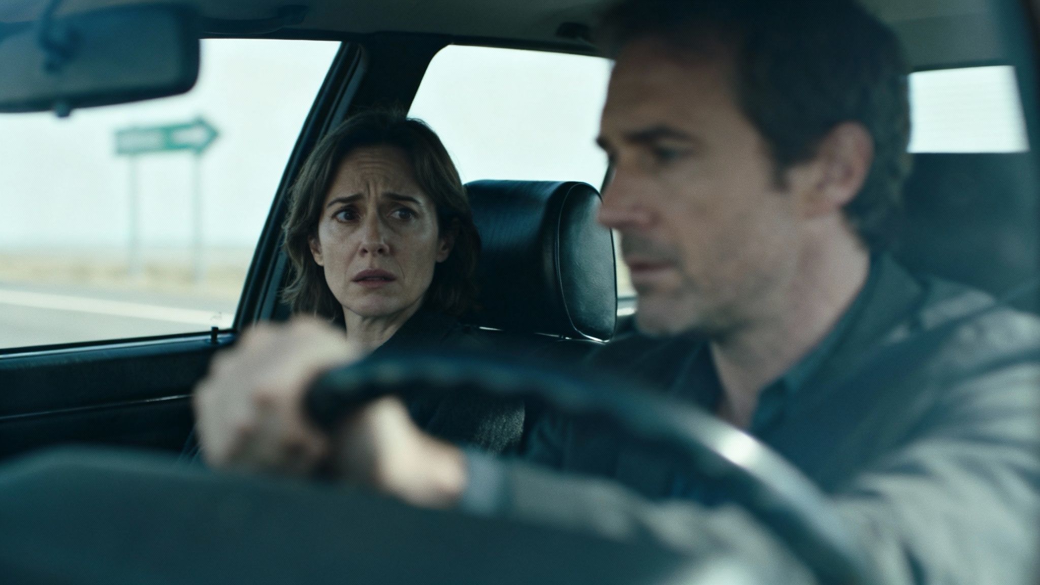 A distressed woman in the passenger seat of a car, as a man drives on a highway.