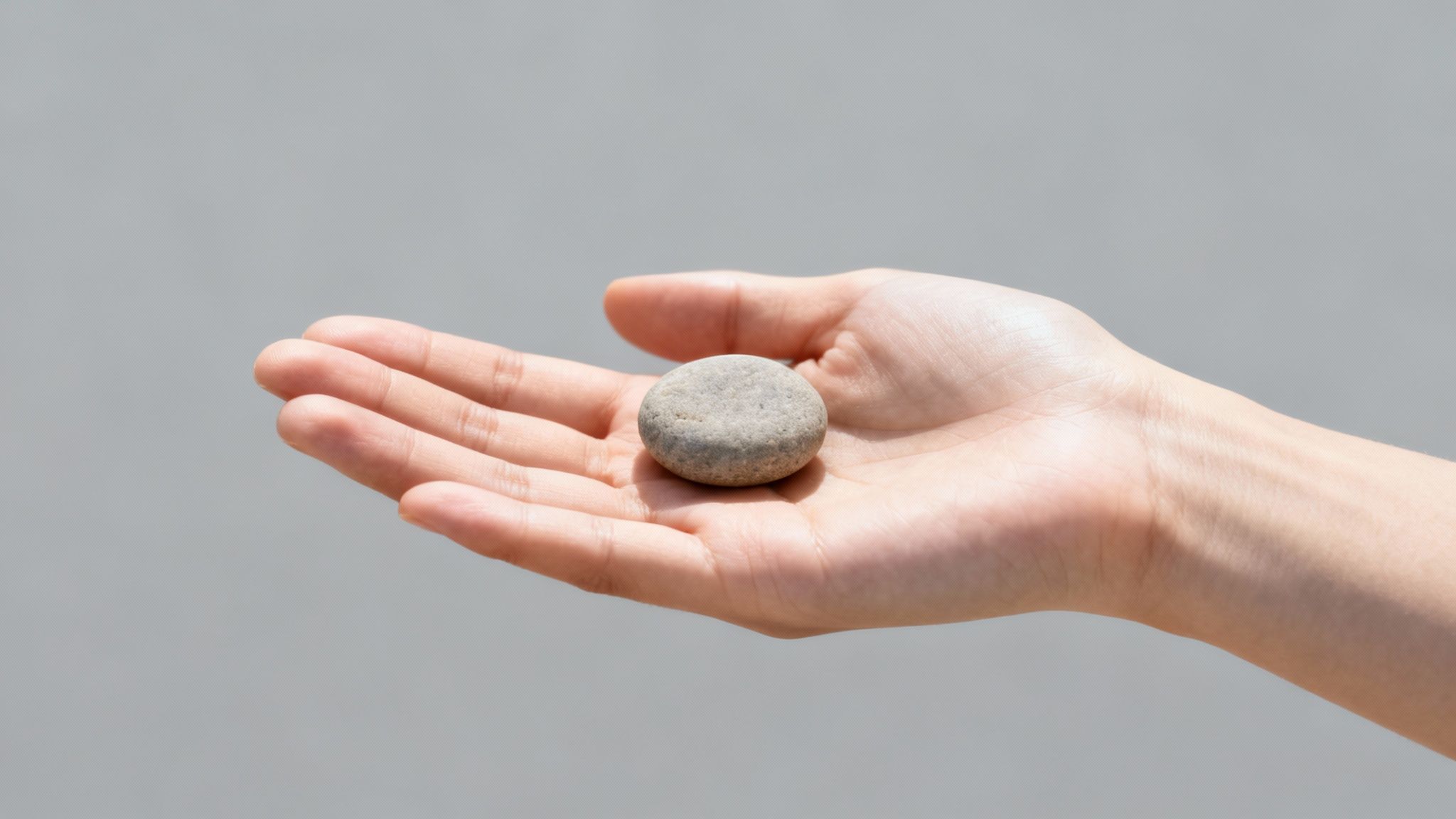 A person's open palm gently holds a smooth, grey, oval-shaped pebble against a plain background.
