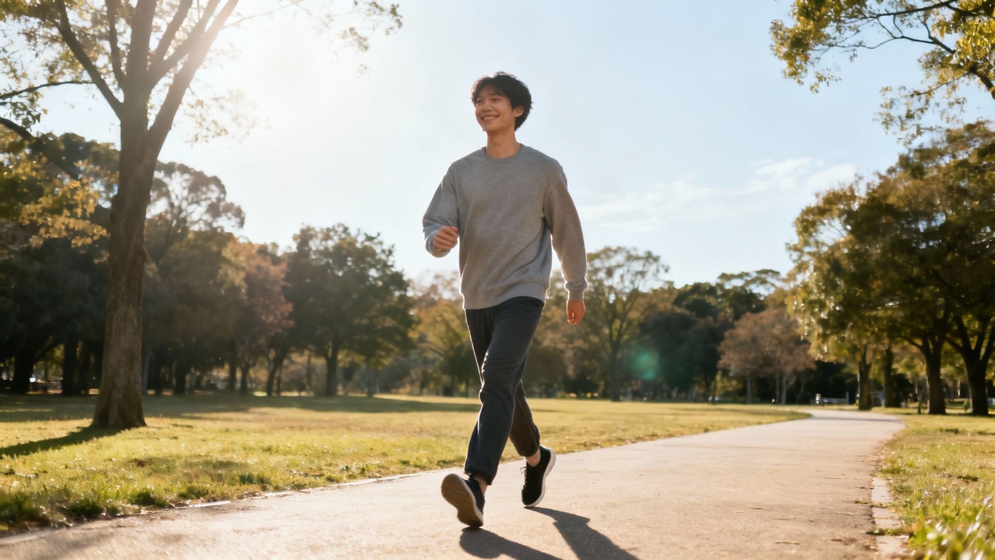 A cheerful young man walks along a park path bathed in bright sunlight.