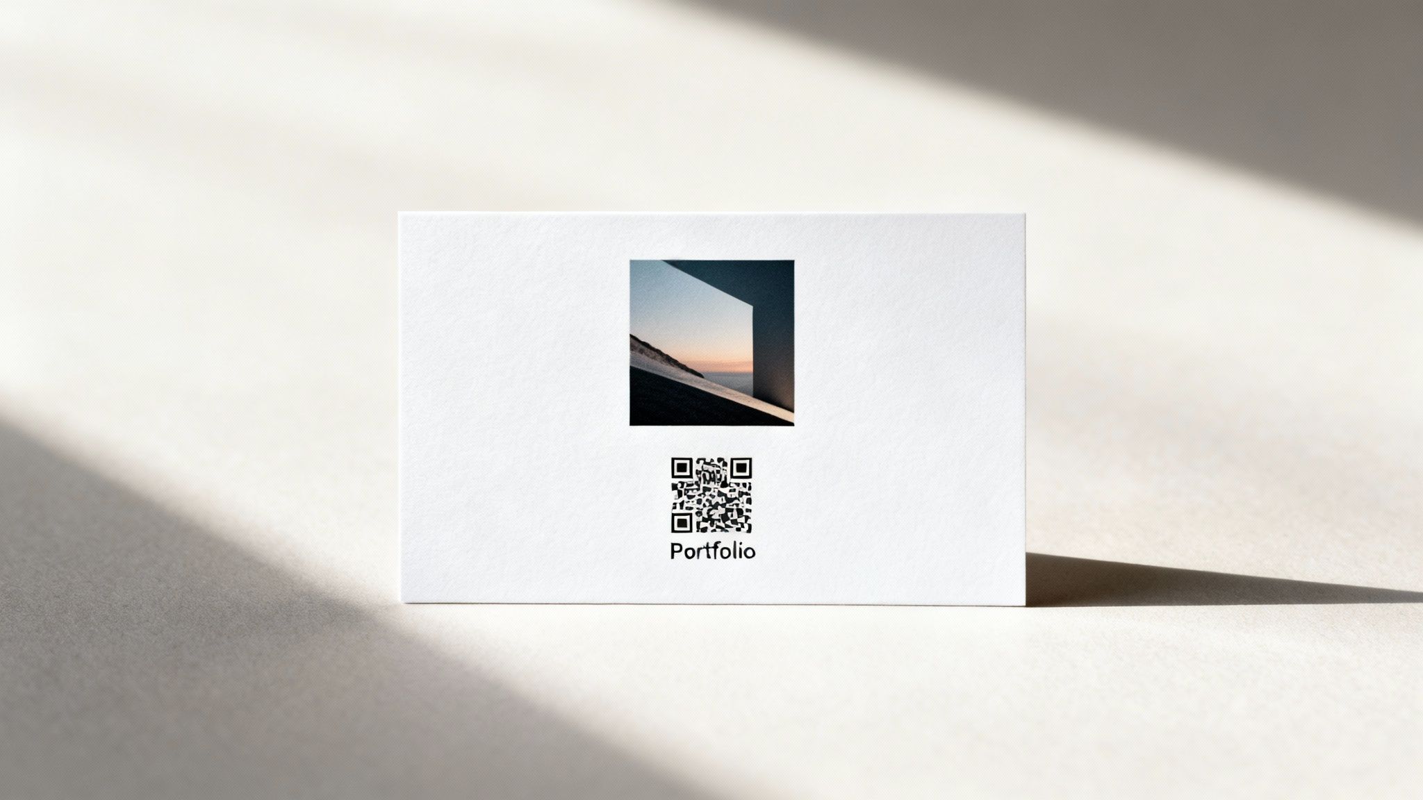 A minimalist white business card featuring a geometric photo and QR code, casting shadows on a textured surface.