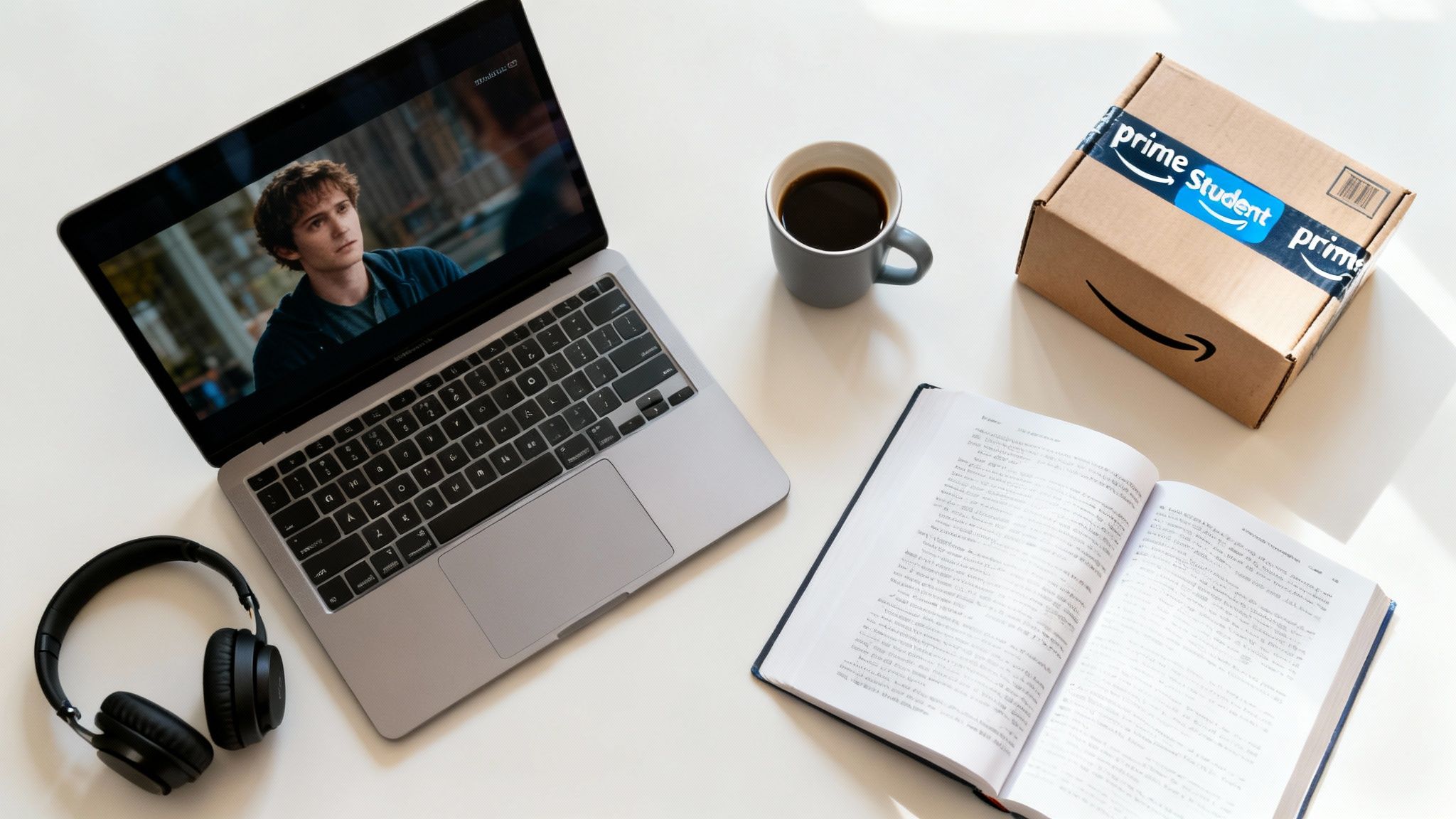 A student's desk with a laptop playing a movie, headphones, coffee, an open textbook, and an Amazon Prime Student box.