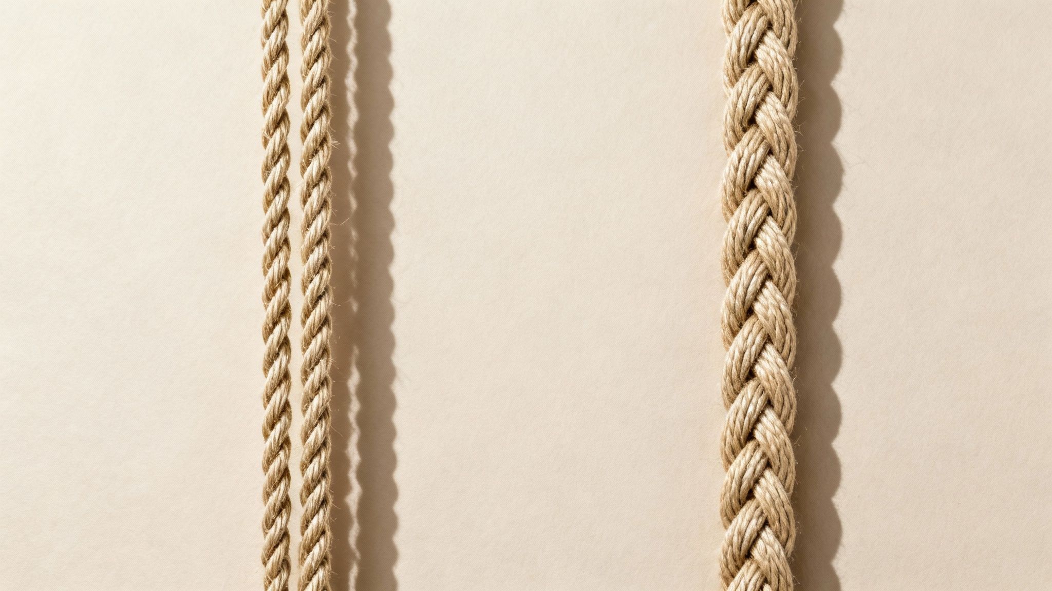 Three natural fiber ropes, two twisted and one braided, cast shadows on a light beige surface.