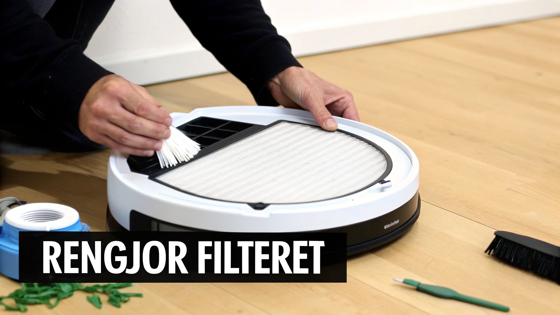 En person rengjør et filter på en robotstøvsuger med en liten børste.