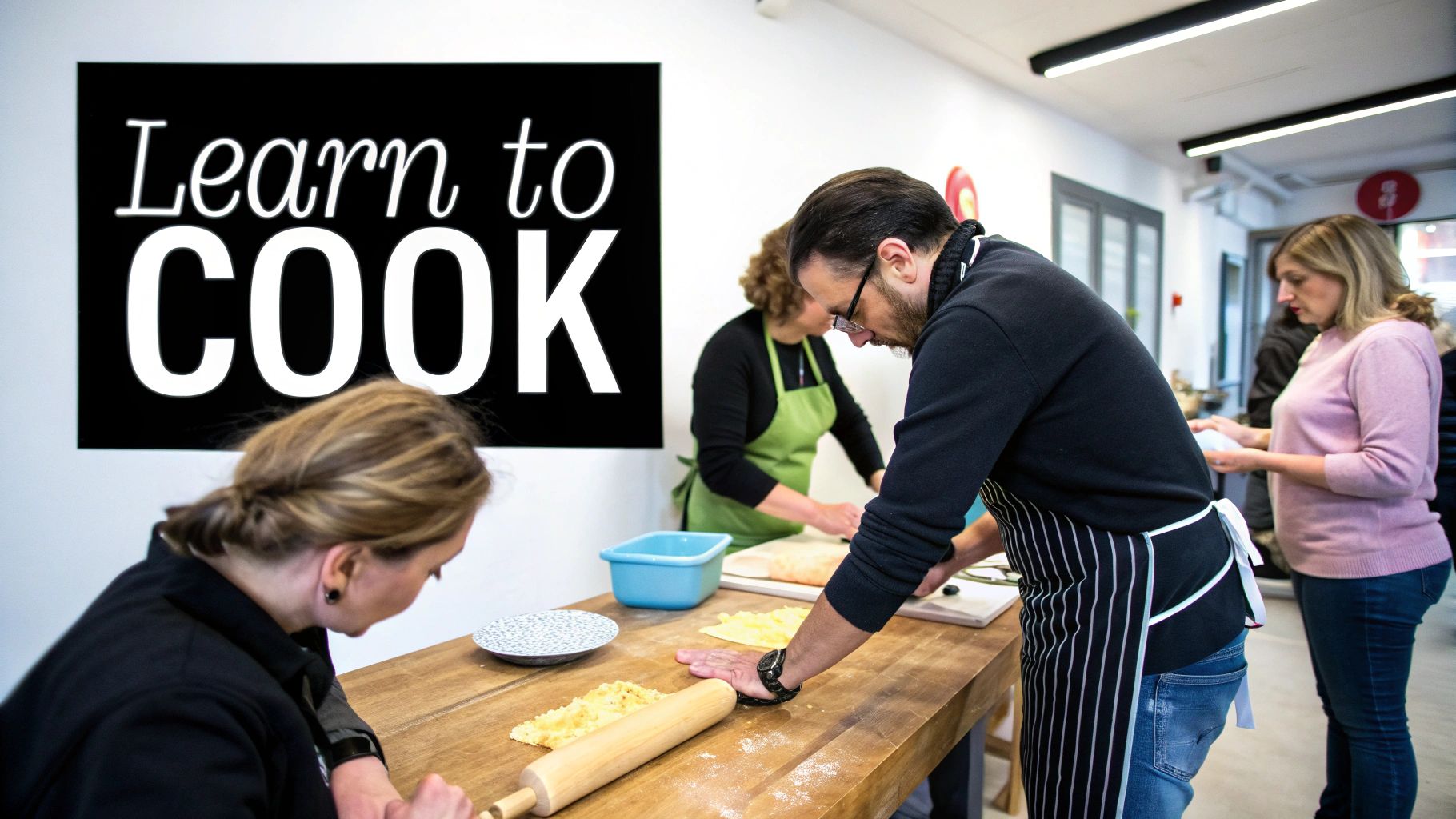 Adults in a cooking class preparing food on a wooden table with a "Learn to COOK" sign.